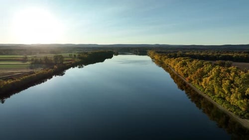 Cinematic drone shot of tranquil river with colorful trees along shoreline. Sunset time in autumn se