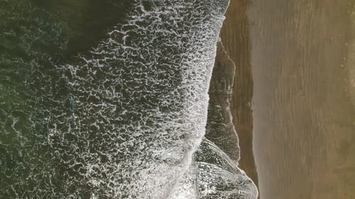 Aerial view of ocean waves washing over sandy shore on a bright sunny day