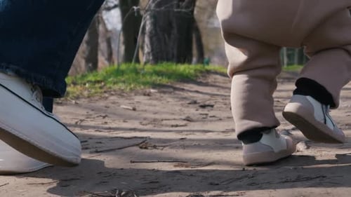 Toddler Taking First Steps on Dirt Path While Parent Follows Closely Behind