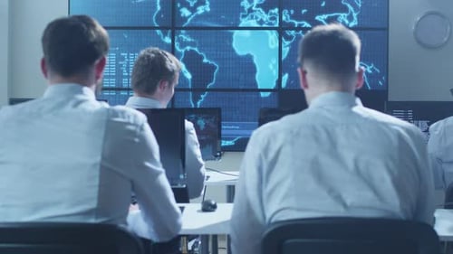 Une équipe de professionnels de la sécurité informatique travaille dans une salle de surveillance lumineuse remplie d'écrans