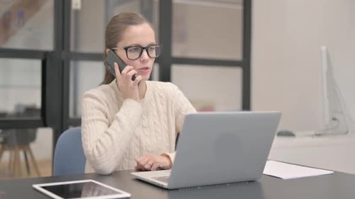 Woman Talking on the Phone While Working on Laptop