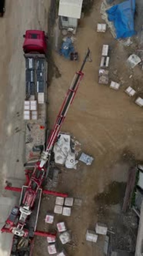 Vertical Video Aerial Construction Scene Crane Unloading Cargo with Builders in Action