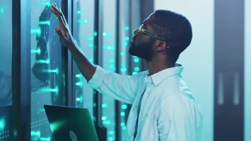 Em uma sala de servidores cheia de tecnologia, um homem se concentra em seu laptop gerenciando as operações
