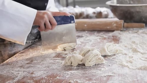 Asian female baker working in bakery kitchen, cutting dough on counter in slow motion