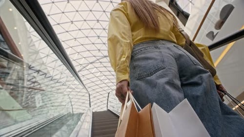 Femme portant des sacs à provisions sur un escalator dans un centre commercial moderne