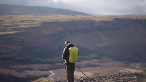 tourist with backpack and tourist sticks on the edge of glymur canyon with mountains on background