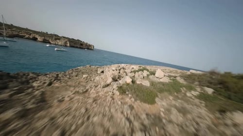 FPV drone shot of steep cliffs and natural stone bridge along the seaside in Cala Varques, Mallorca,