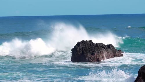 Waves crash against rocky shorelines during bright sunny day at the beach