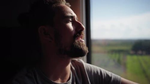 Young Caucasian Man with Beard Looks Out of Train Window Traveler Male Travelling on Railway Pensive