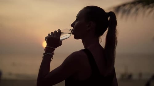 Woman Drinks Water at Beach During Sunrise