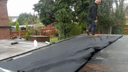 Man Laying Material on Flat Residential Roof
