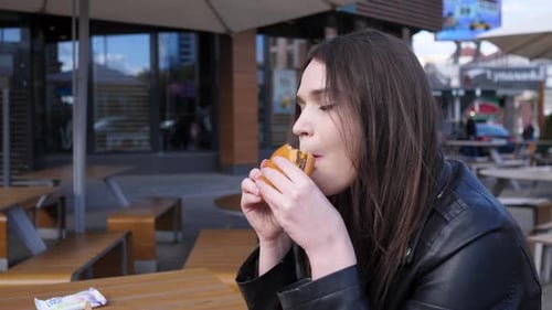 Close Portrait of a Woman Who Eats a Hamburger or Cheeseburger at a Fast Food Place