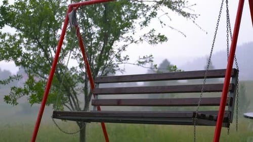 Empty Wooden Swing Gently Swaying in the Summer Rain