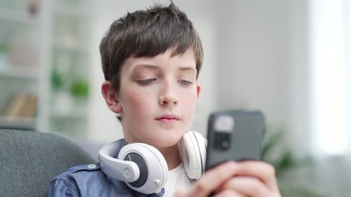 Boy Wearing Headphones Using Mobile Device Indoors