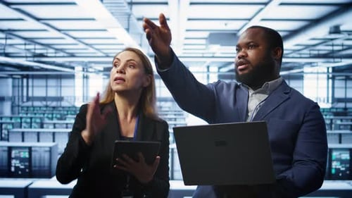 Coworkers in Server Room Optimizing Data Center Tech with Laptop and Tablet