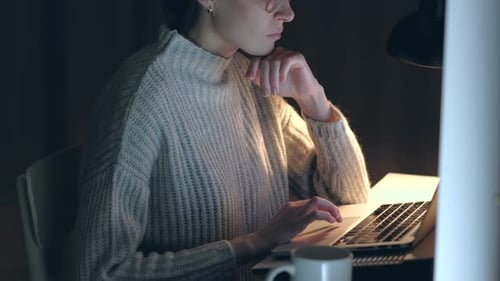 Süße Frau mit Brille surft im Internet in einem dunklen Raum.