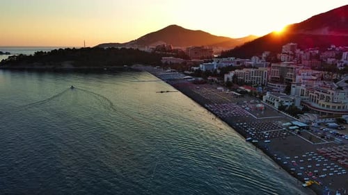 Beach with Sun Umbrellas Sunbeds and People Relaxing in the Town of Becici Near Adriatic Sea Against