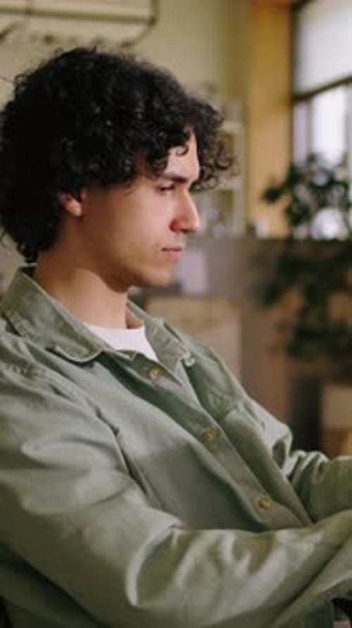 Thoughtful Young Man with Curly Hair Sitting Indoors Focused and Concentrated While Working or