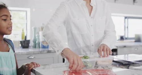 Happy african american mother and daughter packing lunch for school in kitchen, slow motion