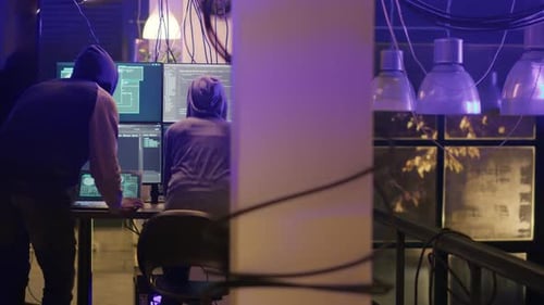 Hooded Figures Hacking Computers in Dark Room