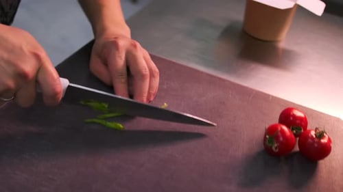 Close-up hands of a chef chopping green onions on a cutting board at a kitchen counter.