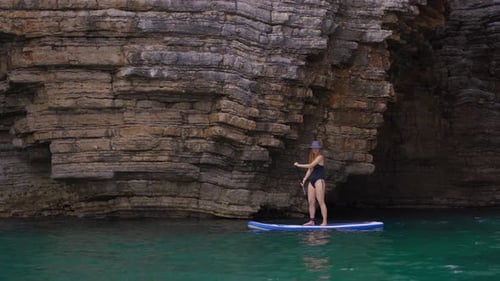 Woman Paddleboarding on Turquoise Water by Rocky Coastline
