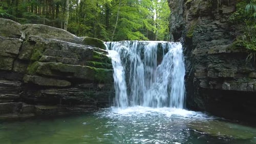 Wasserfall am Gebirgsfluss mit weißem Schaumwasser, das im Sommer von einer Felsformation herunterfällt
