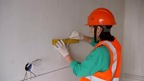 A Woman in a Hard Hat Makes Measurements Using a Construction Level During Finishing Work in an
