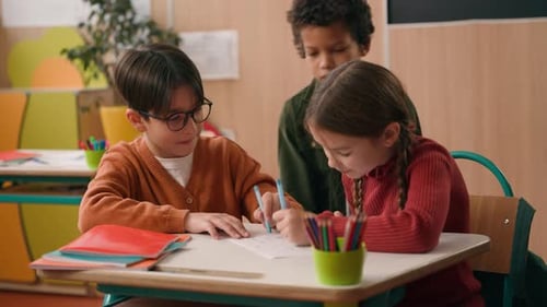 Trois enfants de diversité dans une classe d'école, deux camarades de classe caucasiens, garçon et fille, écrivant, dessinant