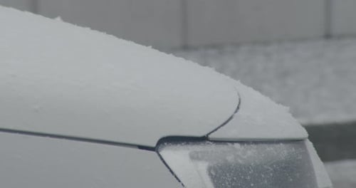 Close up shot of the front part of a car, snow falling