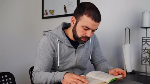 Bearded Adult Reading Book at Table Indoors