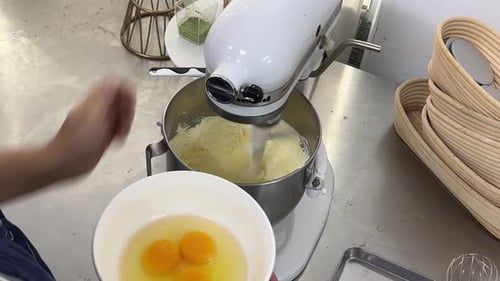 Professional pastry chef adding a bowl of eggs into the cake mixtures, mixing in the mixer and adjus