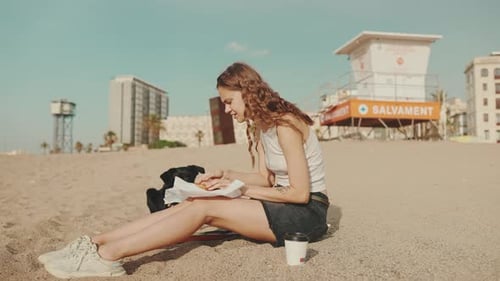 Young Woman Eating Sandwich with Dog on Beach