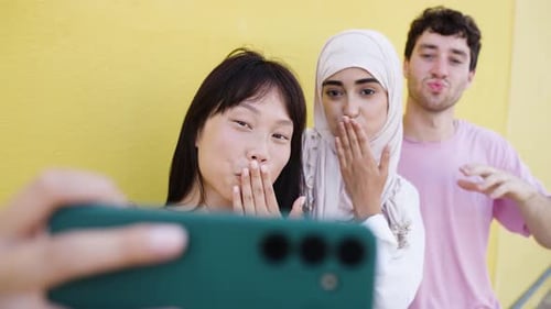 Friends taking phone selfie blowing kisses outdoors