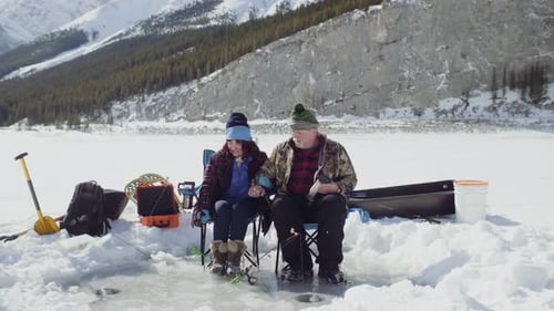 Cheerful Senior Couple Ice Fishing on Frozen Alpine Lake Active