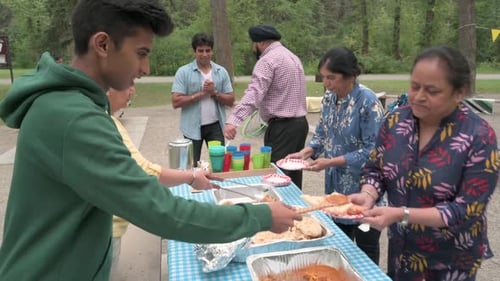Indian Woman And Grandson Serving Food At Picnic In Park