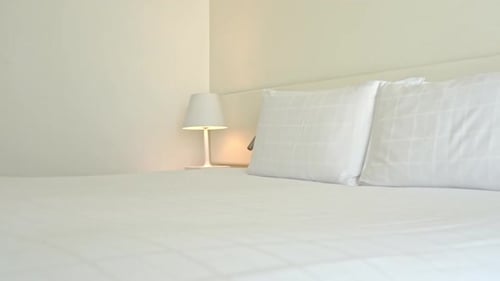 Double bed with white headboard and candid sheets and pillows in hotel room