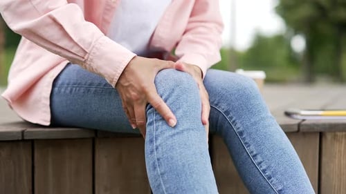 African american female hands massaging knee leg muscles while sitting on bench on street