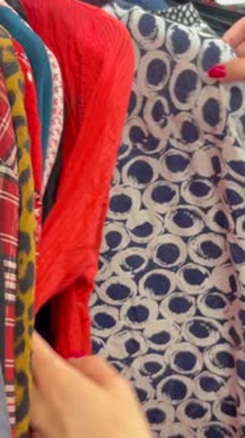 Closeup of Female Hands Choosing Used Clothes on Hangers Black Friday