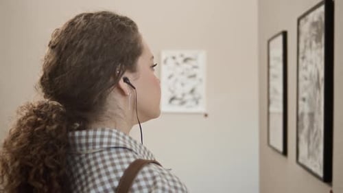 Galeriebesucherin beobachtet abstrakte Gemälde mit Audioguide-Kopfhörern