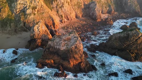 Faszinierende Luftaufnahme eines wunderschönen Felsenstrandes bei Sonnenuntergang mit sanft an der Küste krachenden Wellen