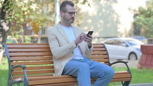 Man Using Smartphone While Sitting on Park Bench