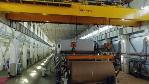 Worker Tears Strip of Paper From Roll Near Machine Tool