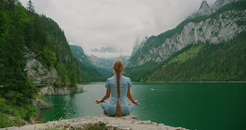 Woman meditating by a serene mountain lake amidst towering cliffs in summer Austria