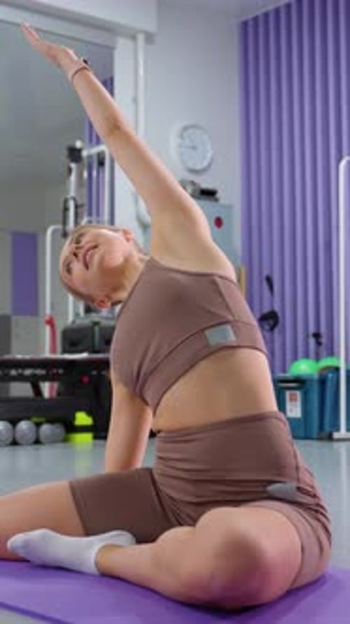 Women Performing Seated Rib Stretch in Gym with Fitness Equipment