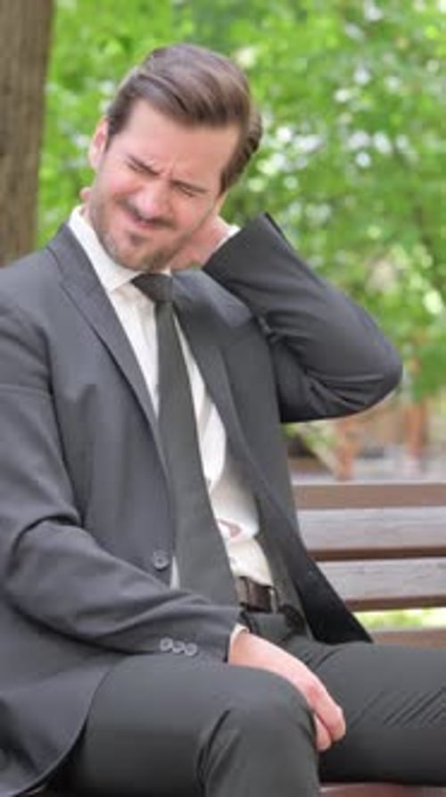 Man in Suit Stretches Neck While Sitting on Bench