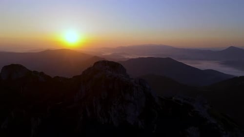 Sunrise Over Mountain Ridge with Golden Light Shining on Peaks and Misty Valley Below