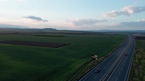 Road with Cars and Trucks on It Passes Through Fields Under a Colored Sky