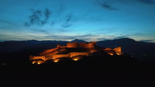 Aerial footage of an illuminated castle on top of the hill at dusk