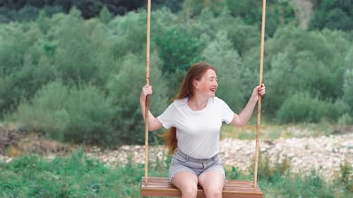 Une fille aux cheveux roux chevauche une balançoire dans la nature